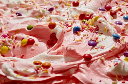 Strawberry and vanilla ice cream topped with sugar-coated chocolate candy and colorful sprinkles for a kids party celebration in a close up background texture