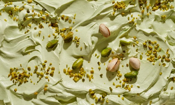 Artisanal homemade green pistachio ice cream with fresh nuts whole, in shells and chopped sprinkled on the surface of the dessert in a full frame background texture