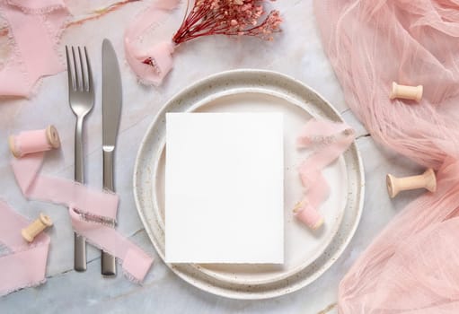 Wedding Table place with a card on porcelain plates with dried pink flowers and silk ribbons top view. Romantic template with vertical blank card flat lay. Invitation or menu card mockup, copy space