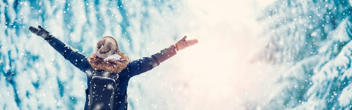 Happy woman with hands up standing in the snowy forest in snowfall. Concept of vacation and holidays.