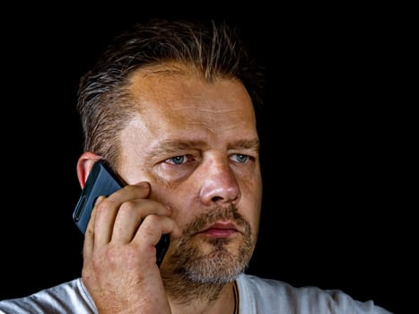 A middle-aged man with a gray beard is talking on a cell phone. Smartphone. Mobile phone. Adult. Cellular. Man's face. Modern technologies. Beard and mustache.