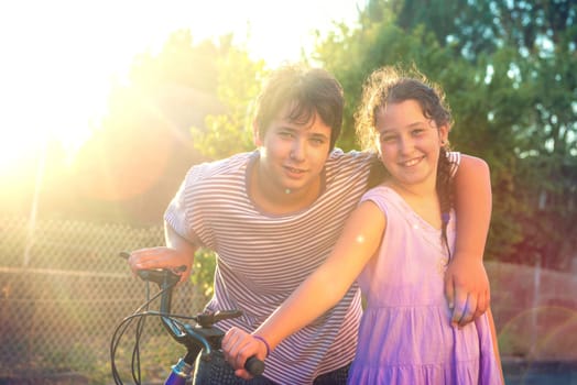 Happy young kid’s couple outdoors at sunset with bicycle