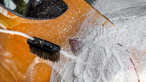 Detail on car rear washed in carwash. Thick shampoo foam spraying on rear light.