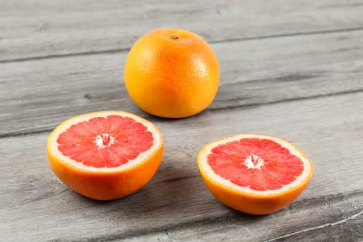 Pink grapefruit cut to half, with other whole citrus in background, placed on gray wood table.