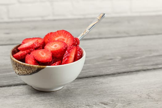 Small bowl of strawberries cut in circle pieces with spoon - ready to eat healthy snack.