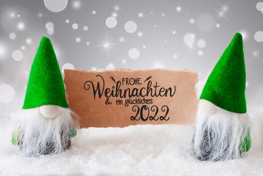 Sign With German Calligraphy Frohe Weihnachten Und Ein Glueckliches 2022 Means Merry Christmas And A Happy 2022. Santa Claus With Green Hat. Snow With Gray Sparkling Background