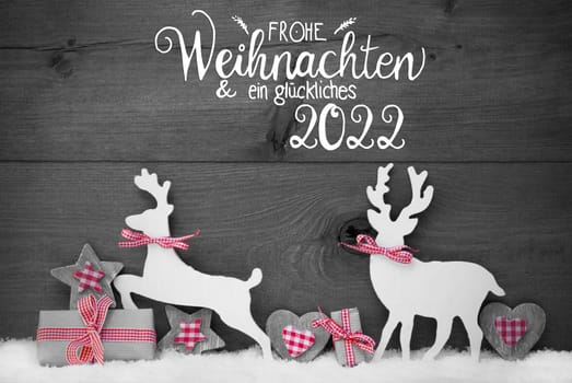 German Calligraphy Frohe Weihnachten Und Ein Glueckliches 2022 Mean Merry Christmas And Happy 2022. Wooden Christmas Ornament Like Present, Heart, And Wooden Deer. Gray Wooden Background With Snow