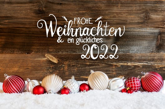 German Calligraphy Frohe Weihnachten Und Ein Glueckliches 2022 Means Merry Christmas And A Happy 2022. Rustic Brown Wooden Backgroud. Red And White Festive Christmas Ball Ornament On Snow.