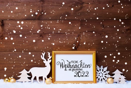 Frame With German Calligraphy Frohe Weihnachten Und Ein Glueckliches 2022 Means Merry Christmas And A Happy 2022. Golden Decoration Like Ball, Tree And Deer. Wooden Background With Snow And Snowflakes