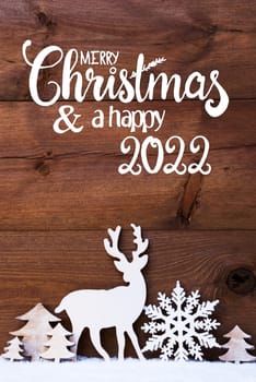 English Calligraphy Merry Christmas And Happy 2022. Christmas Decoration Like Snowflake, Tree And Deer. Brown Wooden Background