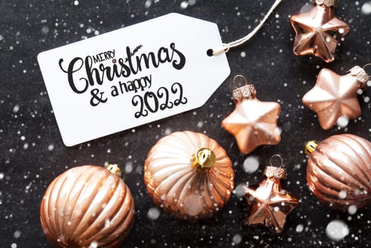 One Label With English Calligraphy Merry Christmas And A Happy 2022. Golden Christmas Ball Ornament On Black Background And Snowflakes