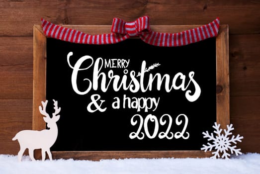 Chalkboard With English Calligraphy Merry Christmas And A Happy 2022. Christmas Decoration Like Deer And Bow. Wooden Background With Snow