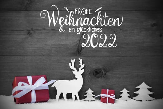 German Calligraphy Frohe Weihnachten Und Ein Glueckliches 2022 Means Merry Christmas And A Happy 2022. Red Christmas Decoration Like Tree, Gift, And Reindeer. Black Wooden Background With Snow