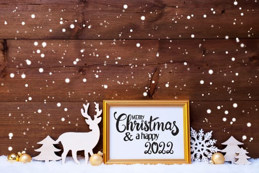 Frame With English Calligraphy Merry Christmas And A Happy 2022. Golden Decoration Like Ball, Tree And Deer. Wooden Background With Snow And Snowflakes