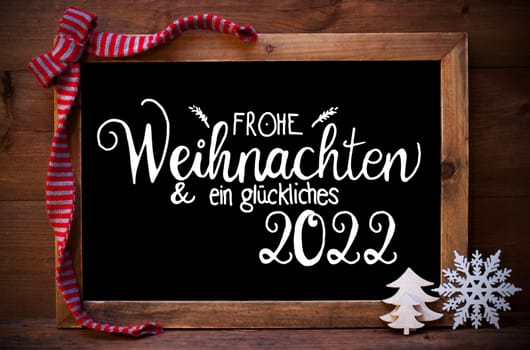 Chalkboard With German Calligraphy Frohe Weihnachten Und Ein Glueckliches 2022 Means Merry Christmas And A Happy 2022. Christmas Decoration Like Tree, Snowflake And Bow. Wooden Background
