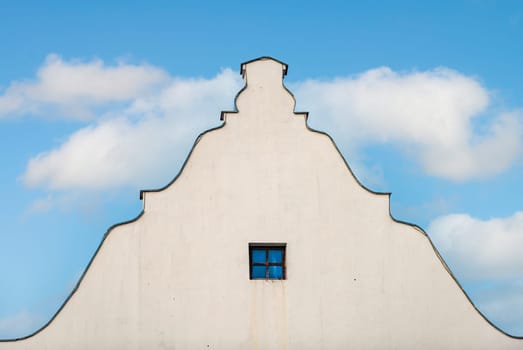 Old building roof and wall with blue cloudy sky in background