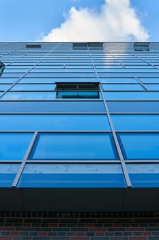 View upwards at the glass facade of a modern office building in Berlin with reflection of blue sky