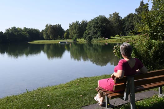Natural springs feed the Germeringer See with water. The local recreation area near the city of Germering is in the Fürstenfeldbruck district in Bavaria. A woman looks out over the water.