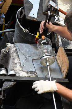 A glassblower shaping and making a drinking glass.