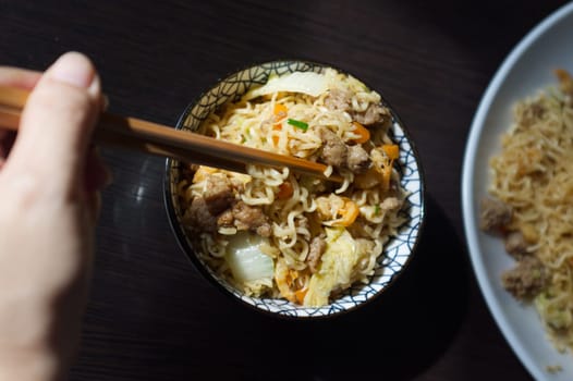 Woman's hand holding chopsticks of instant noodles.