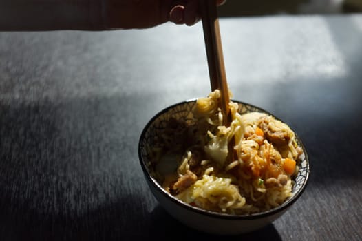 Woman's hand holding chopsticks of instant noodles.
