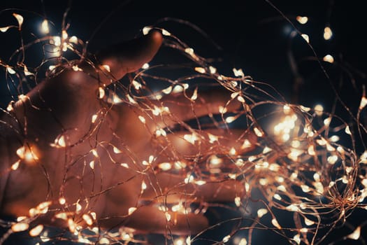 closeup of Caucasian male hand covered in small garland of Christmas lights in the dark