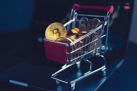 side view closeup cryptocurrency concept of market shopping cart full of bitcoin golden crypto coins standing near a notebook computer screen with trading graphics