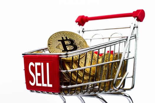 side view closeup cryptocurrency concept of market shopping cart full of bitcoin golden crypto coins with word sell written on front isolated on white background