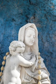 Statue of Our Lady of holy rosary and child Jesus. Blue rustic concrete on background.