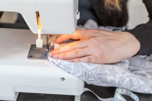 Female hands are sewing at home using a sewing machine closeup. Horizontally.