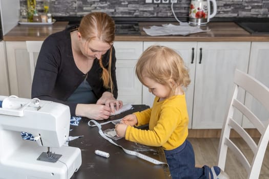 Little son helps his mother in home sewing. Horizontally.