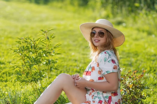 Portrait of attractive  young woman in straw hat sitting outdoors in summer day. Horizontally.