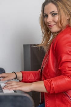 Portrait of smiling  young woman dressed in a red leather jacket playing the piano and looking at the camera. Vertically.