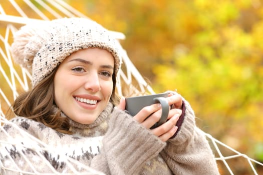 Happy woman holding coffee cup looks away in autumn