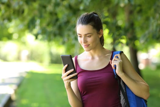 Student walking checking phone in a park