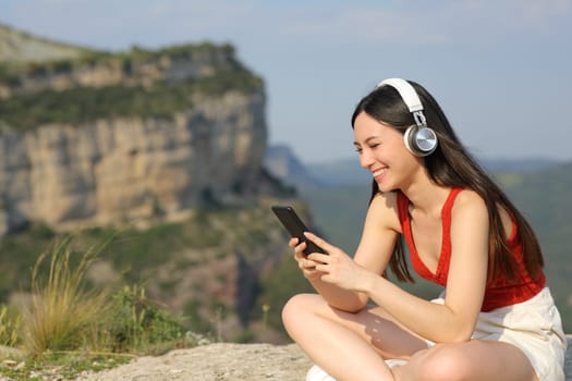 Happy asian woman listening to music in a cliff