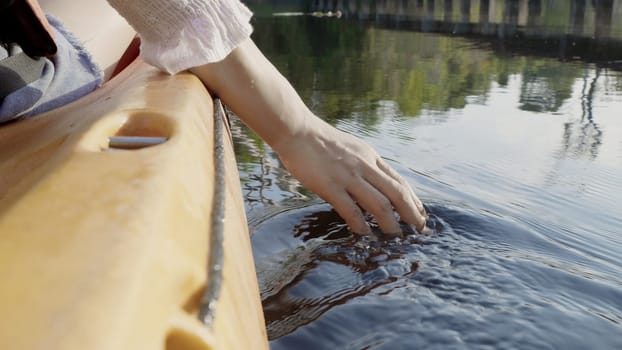 Close up back young adult woman hand on kayaking canoe boat on a lake touching a clear transparent water on summer day, adventure travel leisure enjoying concept, lifestyle sport vacation