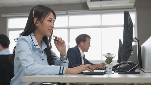 Call center young employee working with headset, Smiling customer support operator team at work surrounded by colleagues working in the office, Helpdesk customer services support agent concept