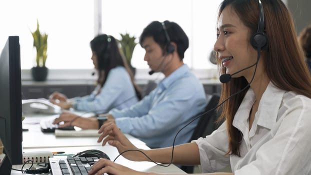 Call center young employee working with headset, Smiling customer support operator team at work surrounded by colleagues working in the office, Helpdesk customer services support agent concept