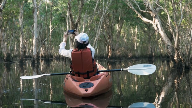 Young adult woman kayaking canoe boat on a lake she take photo natural scenery by smartphone on summer day, adventure travel leisure enjoying concept, lifestyle sport vacation