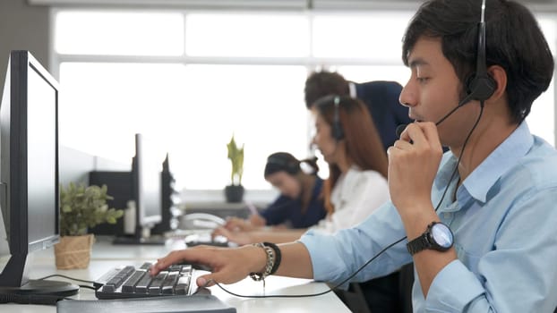 Call center young employee working with headset, Smiling customer support operator team at work surrounded by colleagues working in the office, Helpdesk customer services support agent concept