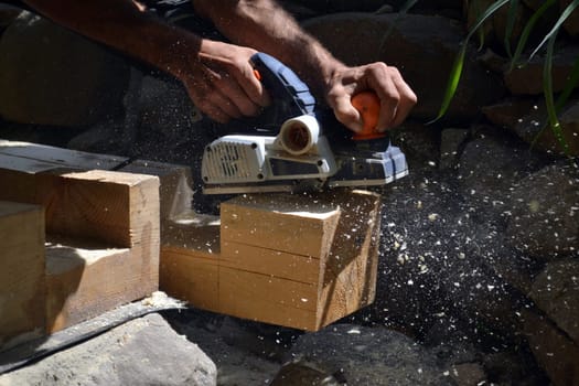 Hands of a carpenter working with electric planer tool