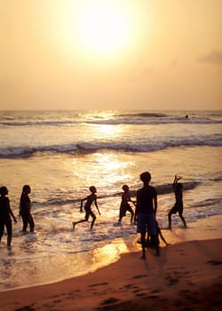 Kalutara, Sri Lanka - April 15, 2017: Silhouettes of people, mostly kids playing on the beach, sea and golden sunset afternoon light in background.