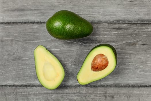 Table top view on avocado cut in half, with whole one above, placed on wood desk.