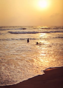 Kalutara, Sri Lanka - April 15, 2017: Silhouettes of two local boys playing in the sea, golden sunset afternoon light in background.