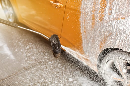 Foam and soap spraying from the brush onto rear wheel of car washed in carwash.