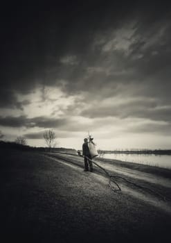 Lonely nomad man carrying firewood for heating, walking a country road. Moody and dramatic scene, black and white vertical background