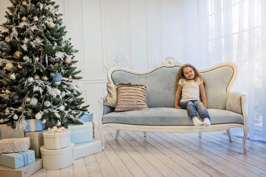 Beautiful girl sitting on the sofa near christmas tree