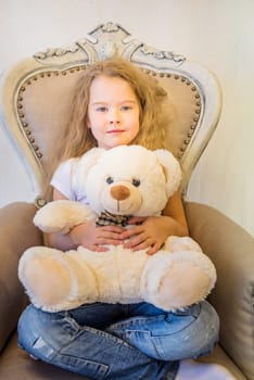 Cute girl in casual clothes sitting in the armchair and hugging toy