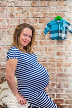 Beautiful pregnant woman sitting near the brick wall.
